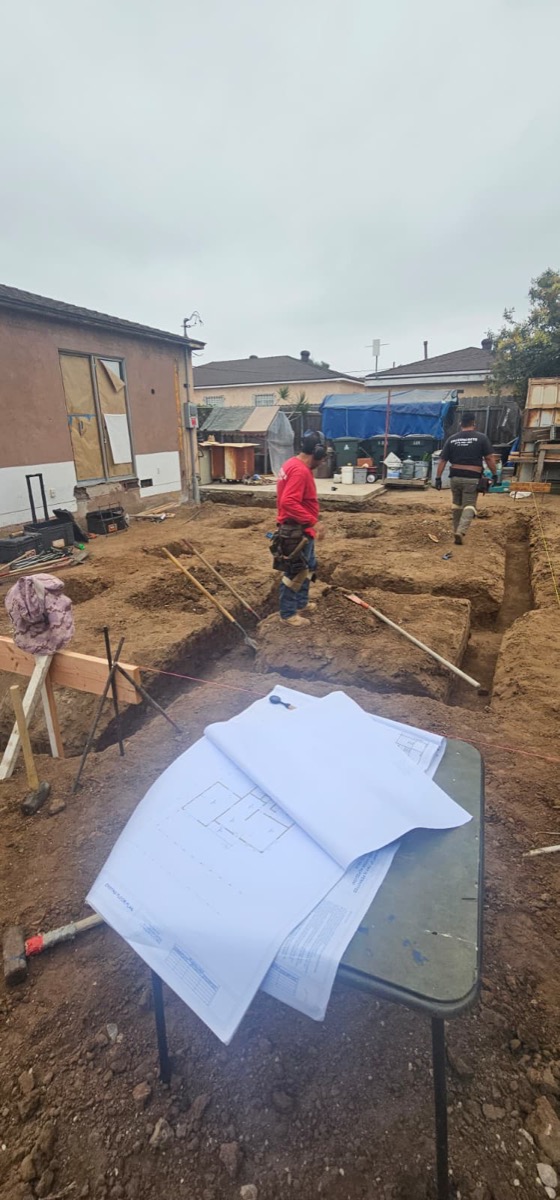ADU site excavation with blueprints on table and crew digging
