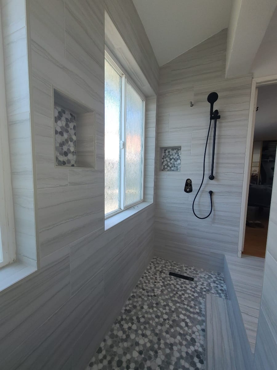 Walk-in shower with gray linear tile, pebble floor and natural light