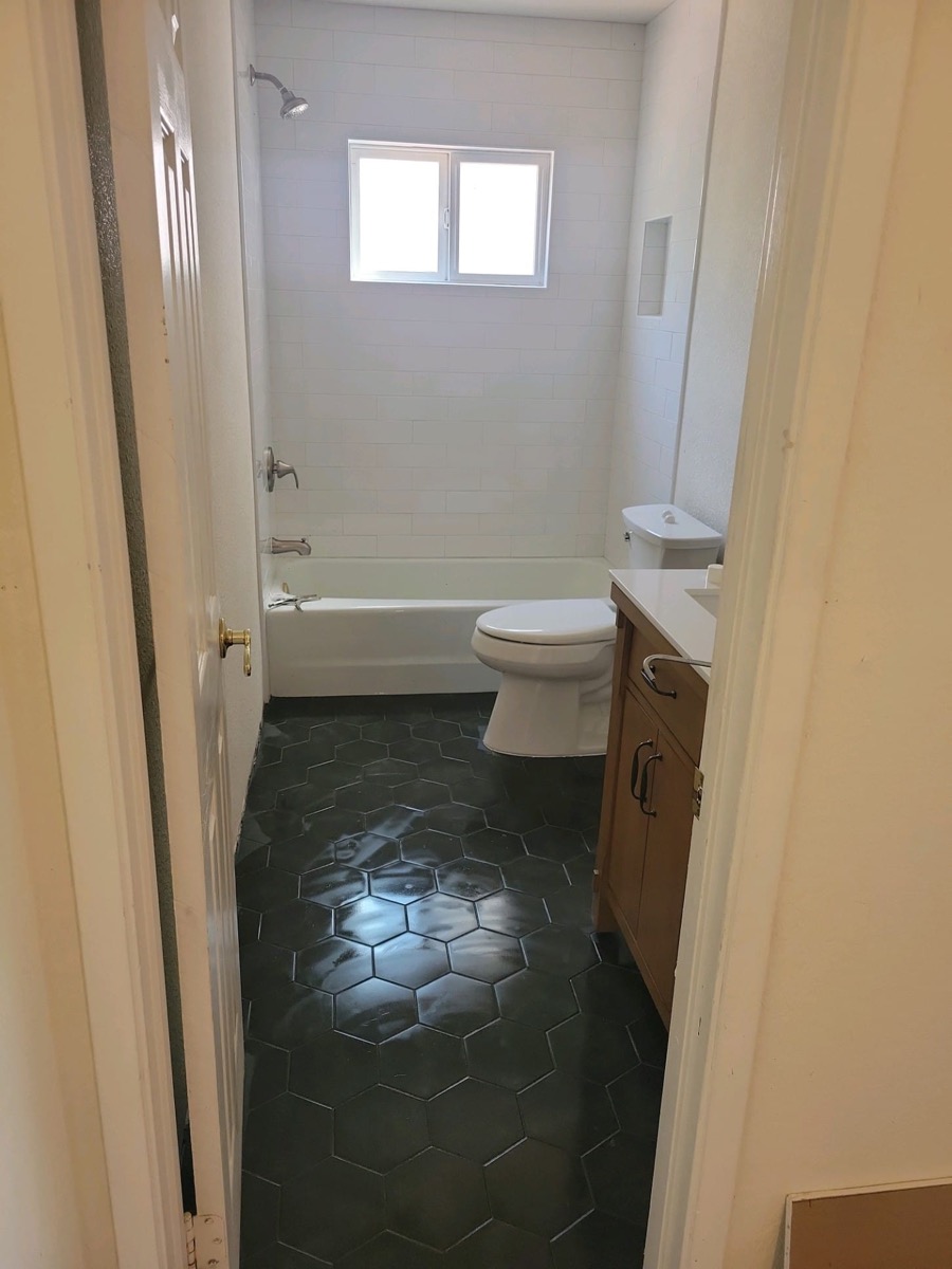 Full bathroom remodel with black hexagon tile floor and tub surround